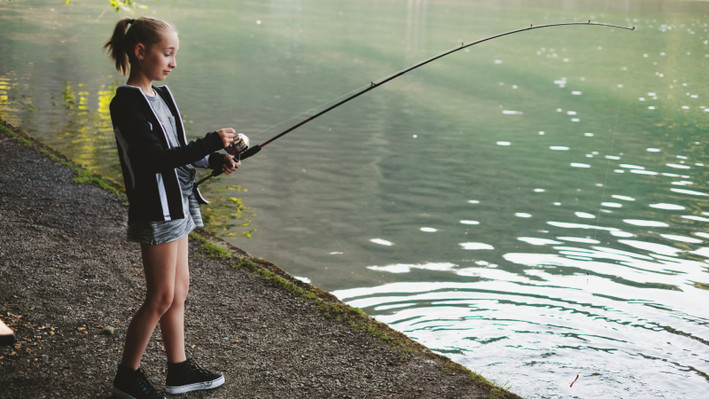 Teenage girl standing by water with a fishing pole