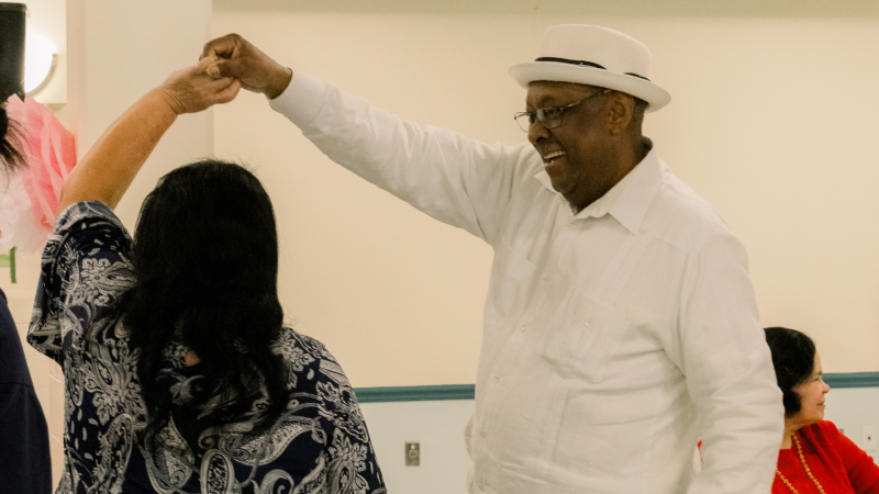 Seniors dancing with their hands holding and up high as the female twirls and the male smiling