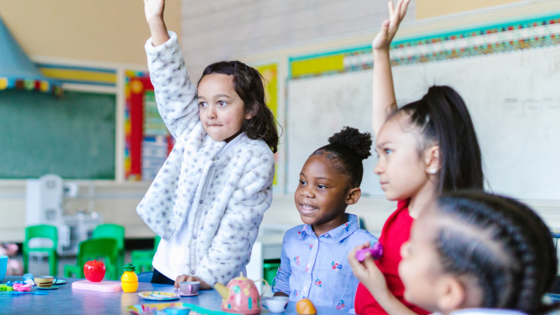 A group of four elementary schoolers raising their hands. 