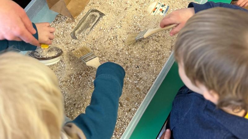 Two young children are digging in a small bin as they learn about archaeology. 