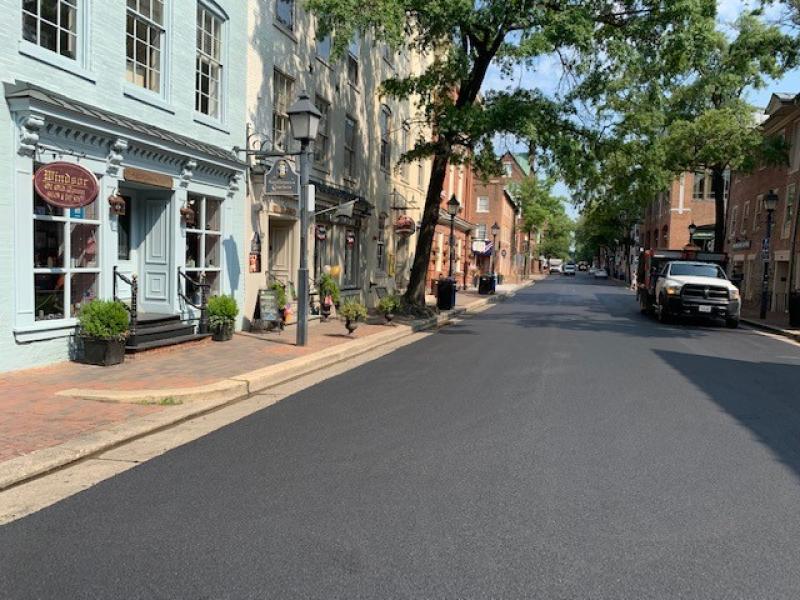 A white work truck is parked on the black asphalt of a newly paved street block