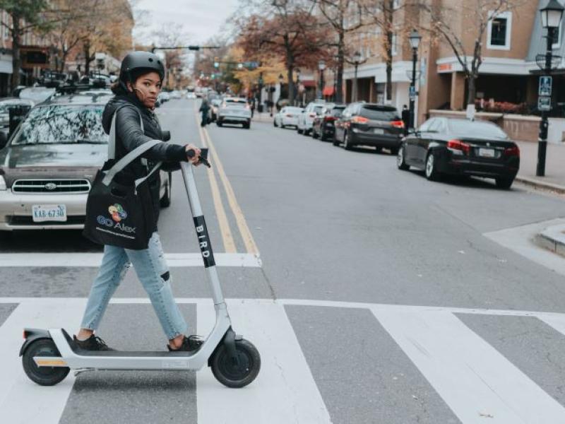 Photo of a person walking a Bird scooter across King Street, in crosswalk