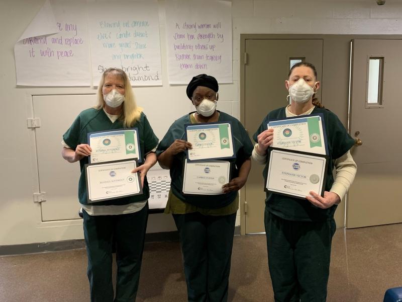 three inmates holding certificates of achievement