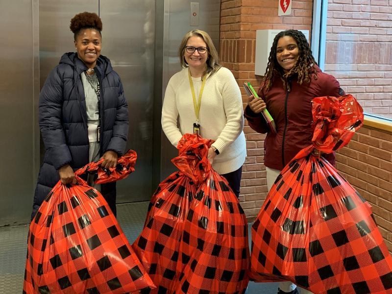 three professional staff members smiling and each holding an oversized plastic gift bag with a red and black design