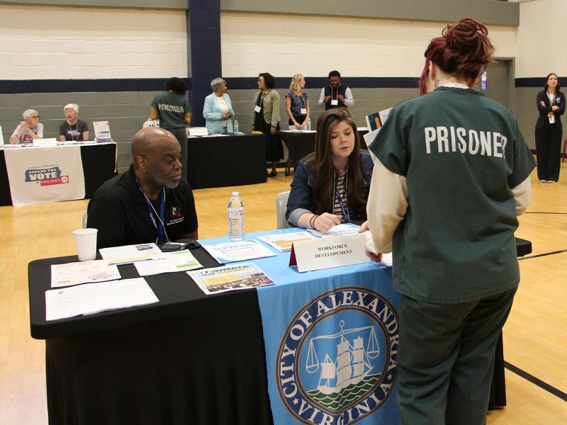 Inmate in green uniform that says Prisoner on the back speaking with two members of the Workforce Development team at the Reentry Resource Fair