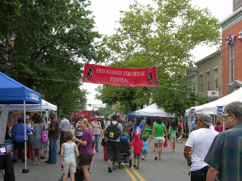 Adults and children walk in the middle of the street between vendor tents at the Friendship Firehouse Festival.  