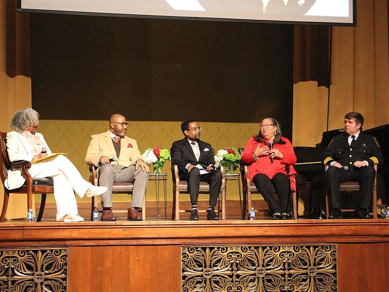 five people seated and talking on a stage