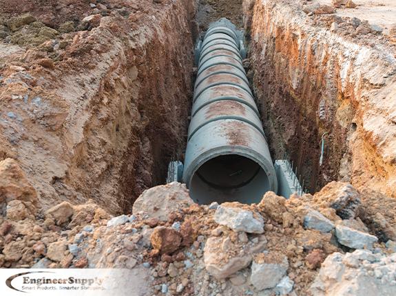 A photo of an open trench with a large concrete pipe installed in the bottom of the trench.