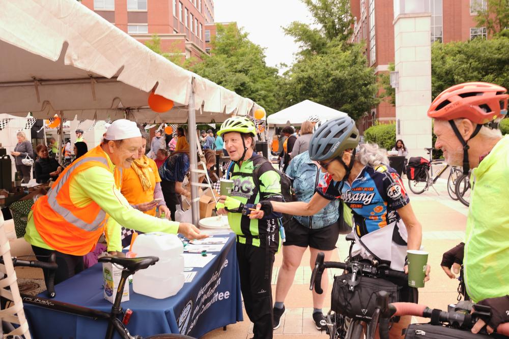 Three cyclists receive informational material from volunteer.
