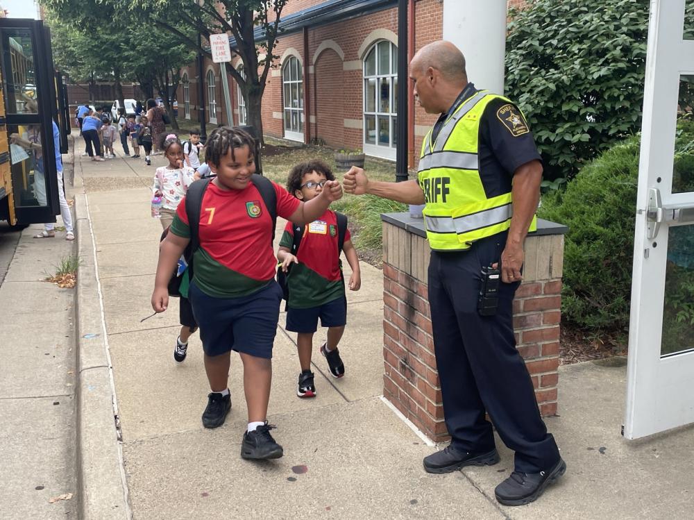 deputy wearing bright yellow traffic share fist bump with a student arriving at school