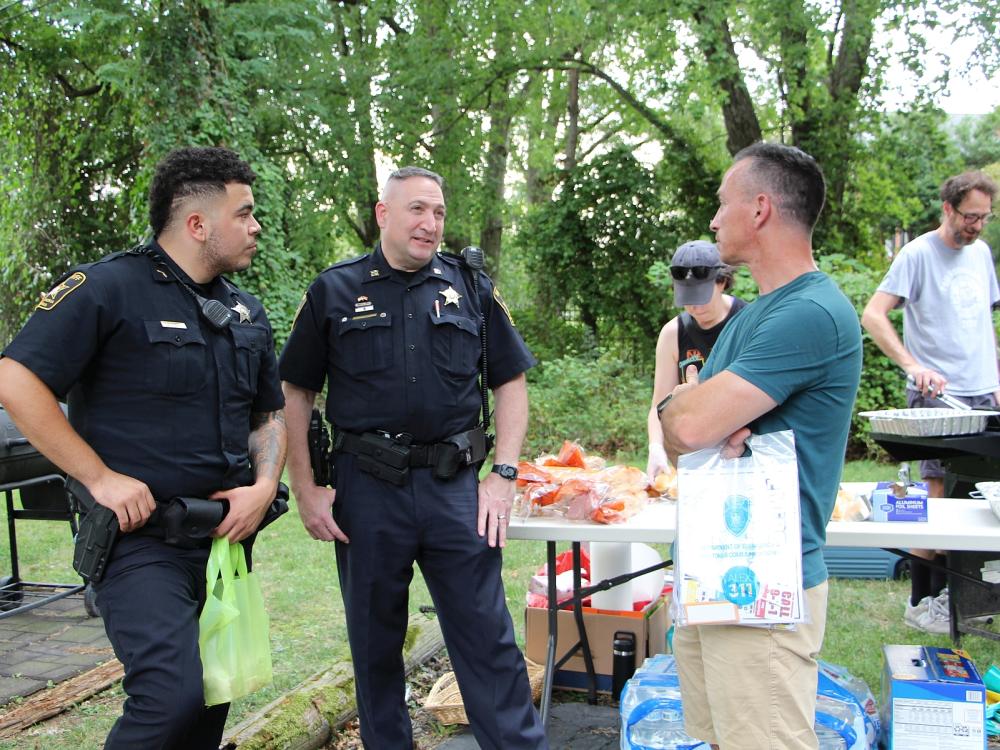 Two deputies talking with man with people grilling in the background at a National Night Out event in the Brookville-Seminary Valley neighborhood