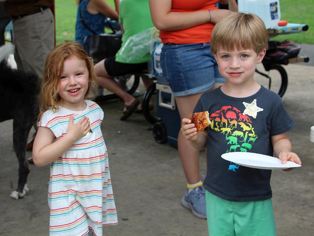 Two small children, each wearing a junior deputy sticker, smiling at a National Night Out event.