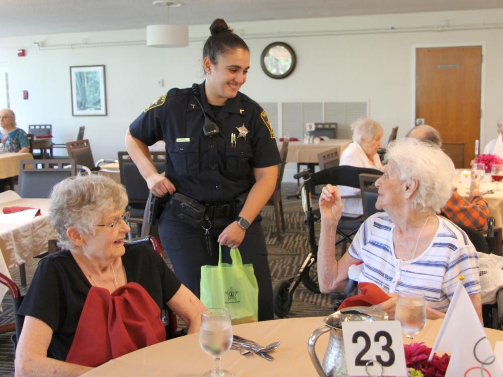 Deputy standing and talking with two residents of The View who are seated at dining table.