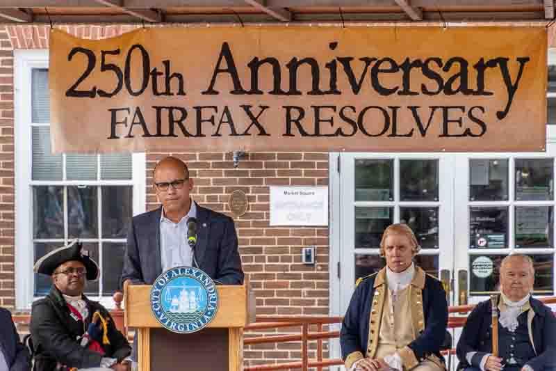 Mayor Justin Wilson at podium with men in Colonial attire seated on stage