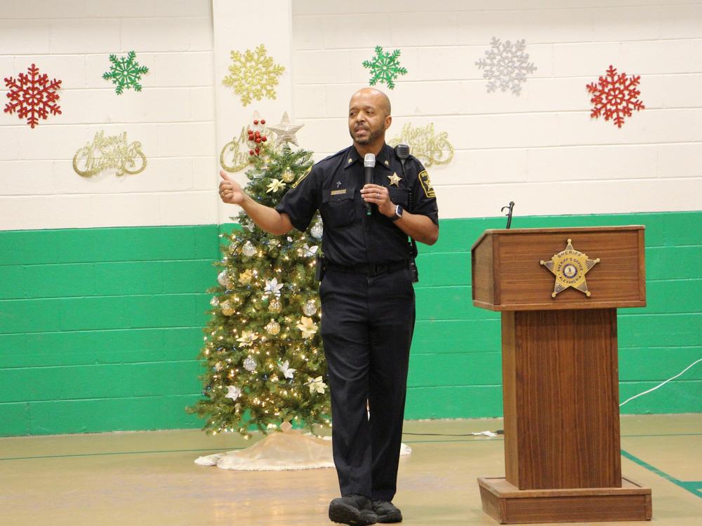 deputy in a blue information holding a microphone and speaking with a Christmas tree and decorations in the background