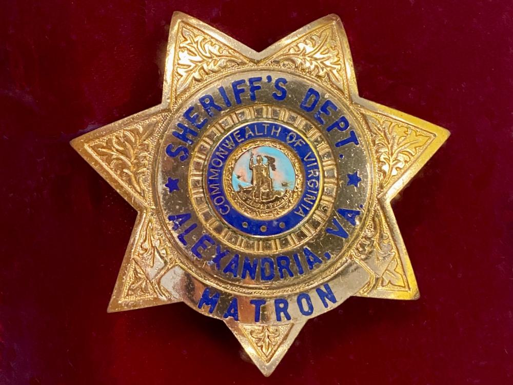 seven point gold tone badge for "Matron for "Sheriff's Dept" in "Alexandria, VA" with seal of the Commonwealth of Virginia in center, on a red velvet background