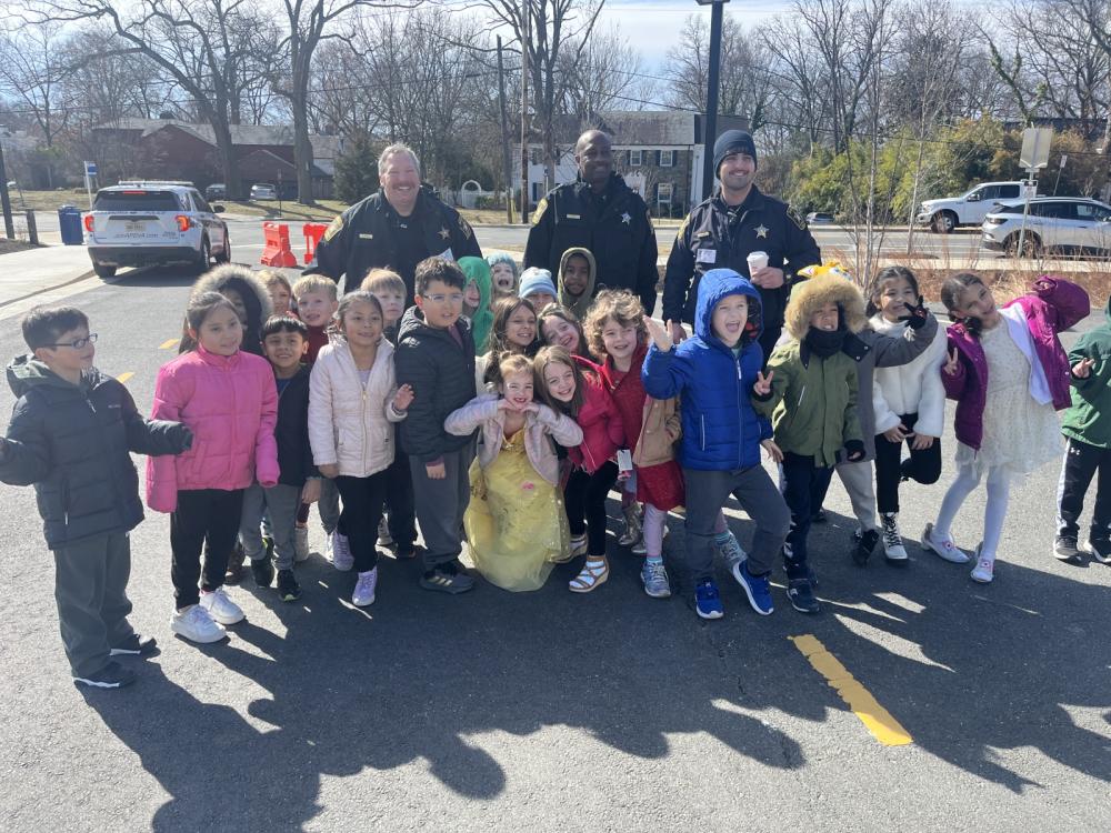 Three deputies in blue uniforms standing with approximately 15 small children in front of them oustide a school