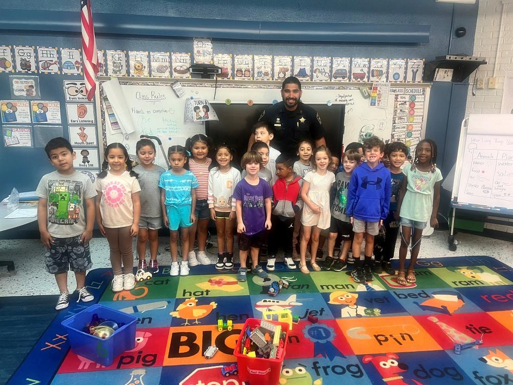 deputy in blue uninform standing with several elementary students in a classroom