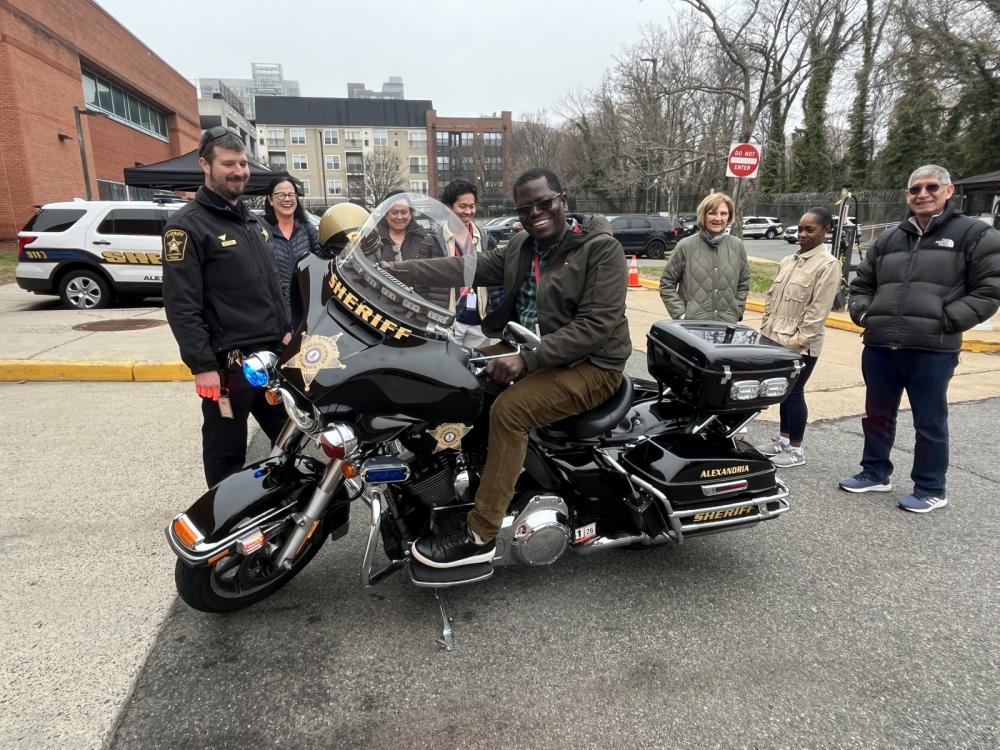 Deputy in blue uniform allowing community member to sit on his agency motorcycle while other community members look on