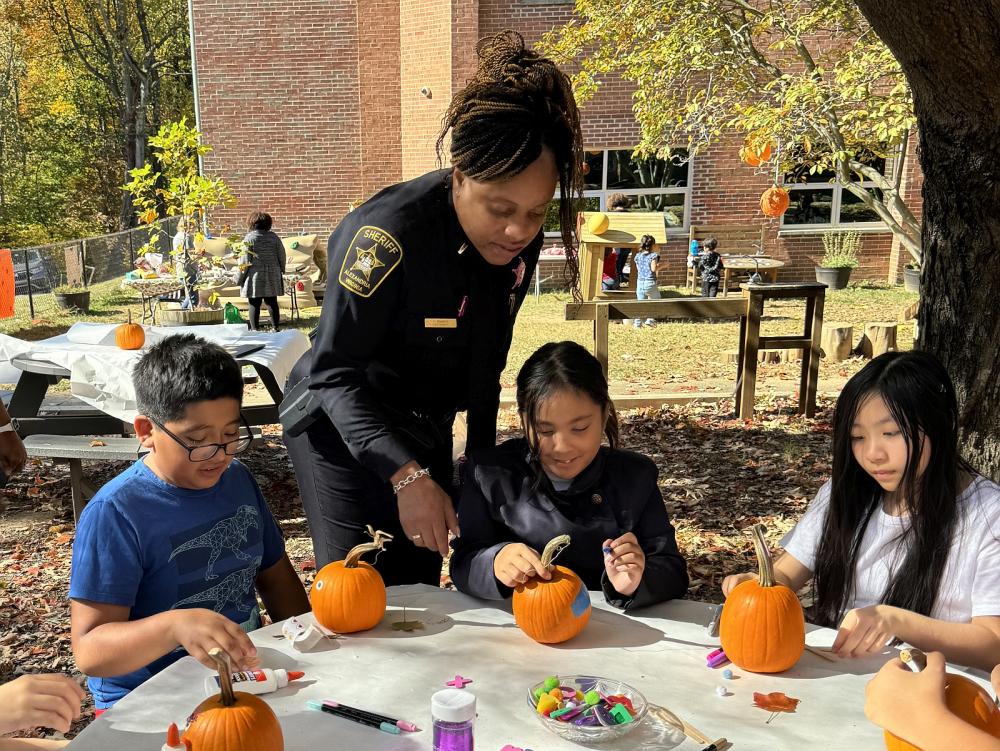 Deputy in a blue uniform helping three children decorate small pumpkins for Halloween