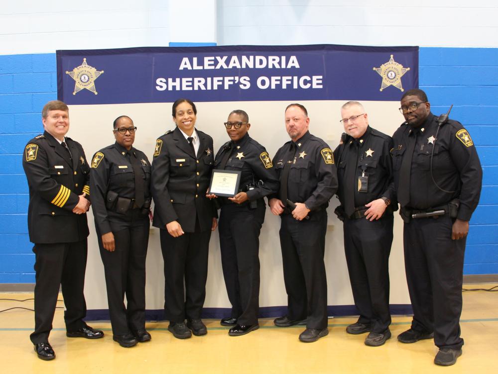 Sheriff and six deputies, all wearing blue uniforms and deputy in the middle is holding an award plaque