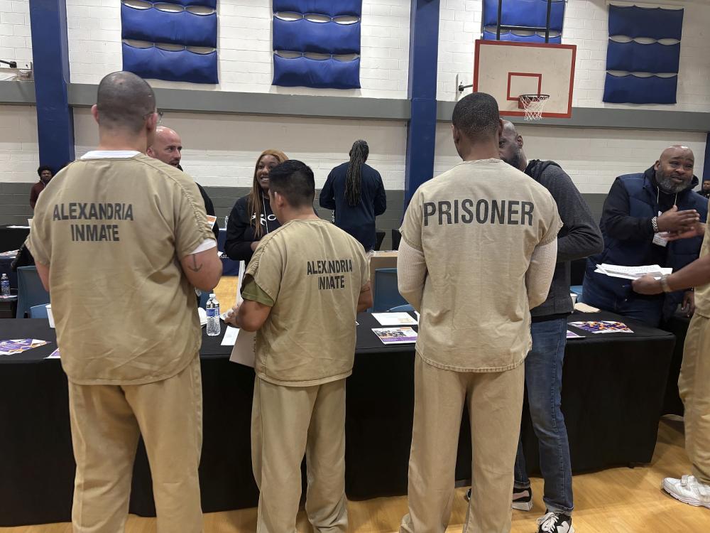 Three inmates in tan jumpsuits seaking with members of a community organization in a gym