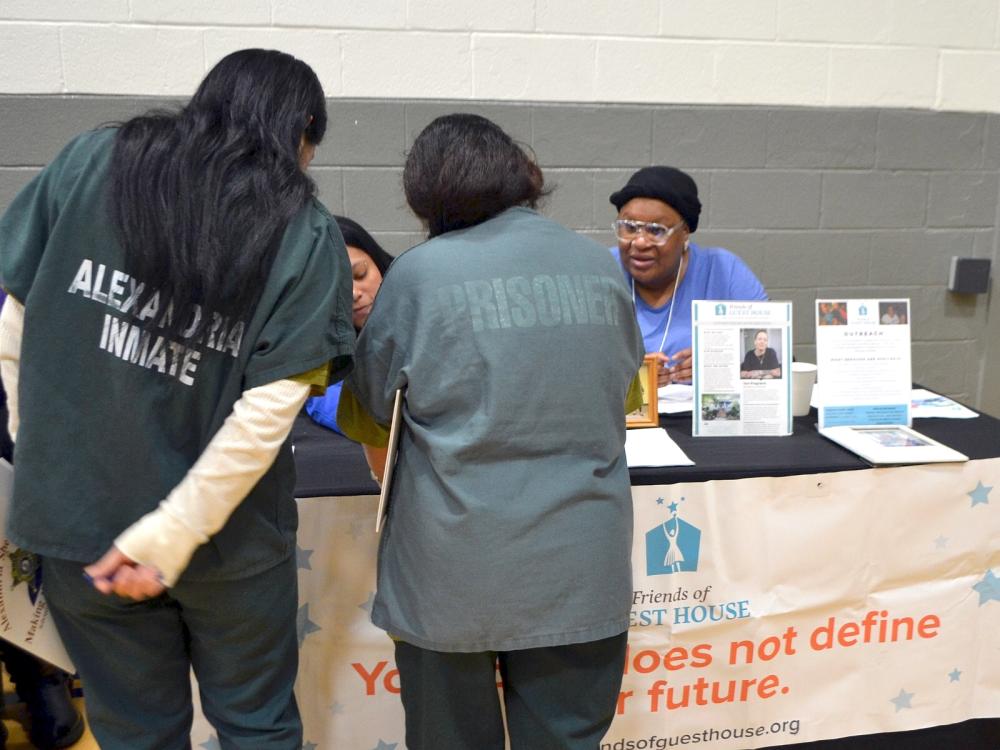 Two inmates in green jumpsuits speaking to exhibitors seated at a table