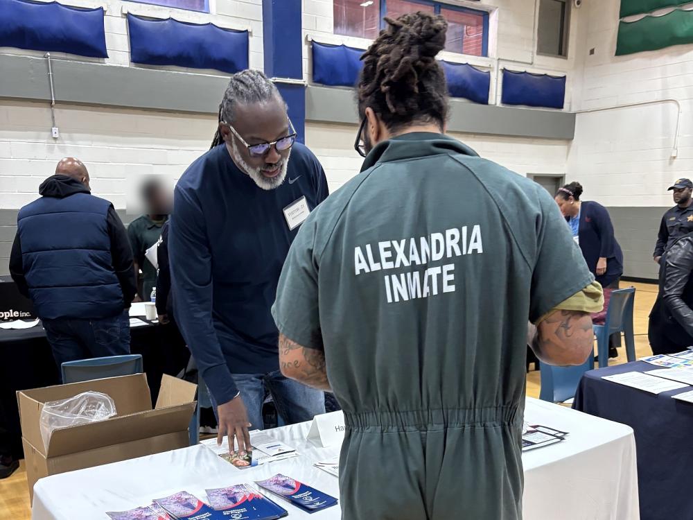 Inmate in a green jumpsuit speaking with an exhibitor who had brochures in front of him