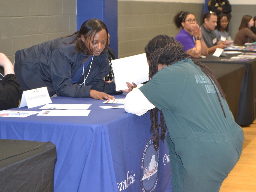 Inmate in a green jumpsuit speaking with a Virginia Probation and Parole staff member across a table 
