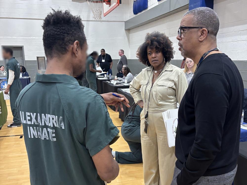 Inmate in a green jumpsuit speaking with two civilian Sherif's Office staff members at the reentry resource fair