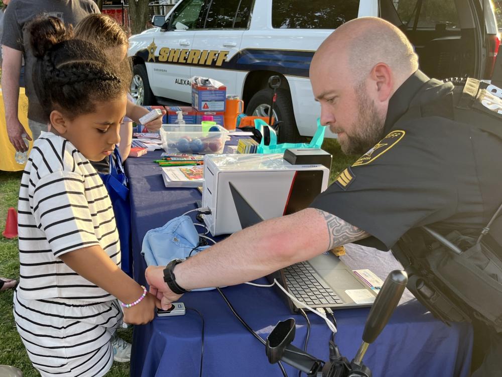 Deputy sheriff in blue uniform taking a digital fingerprint of a small child at a community event