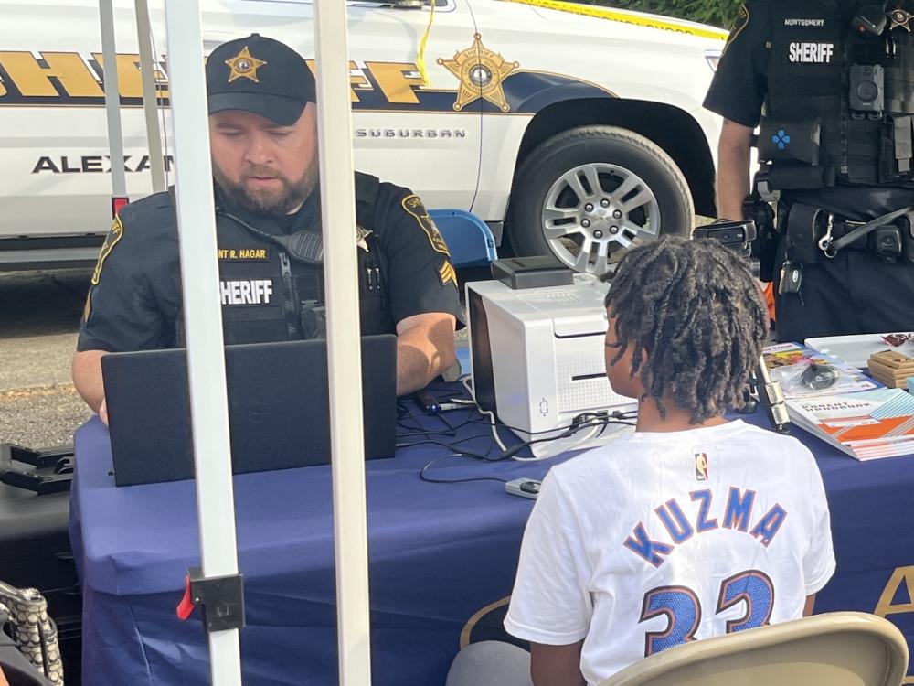 Deputy in blue uniform with a laptop and a child wearing an NBA player shirt facing him