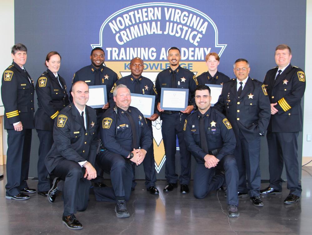 Sheriff with four recruits and several commanders and training staff members, all in blue uniforms with ties and smiling