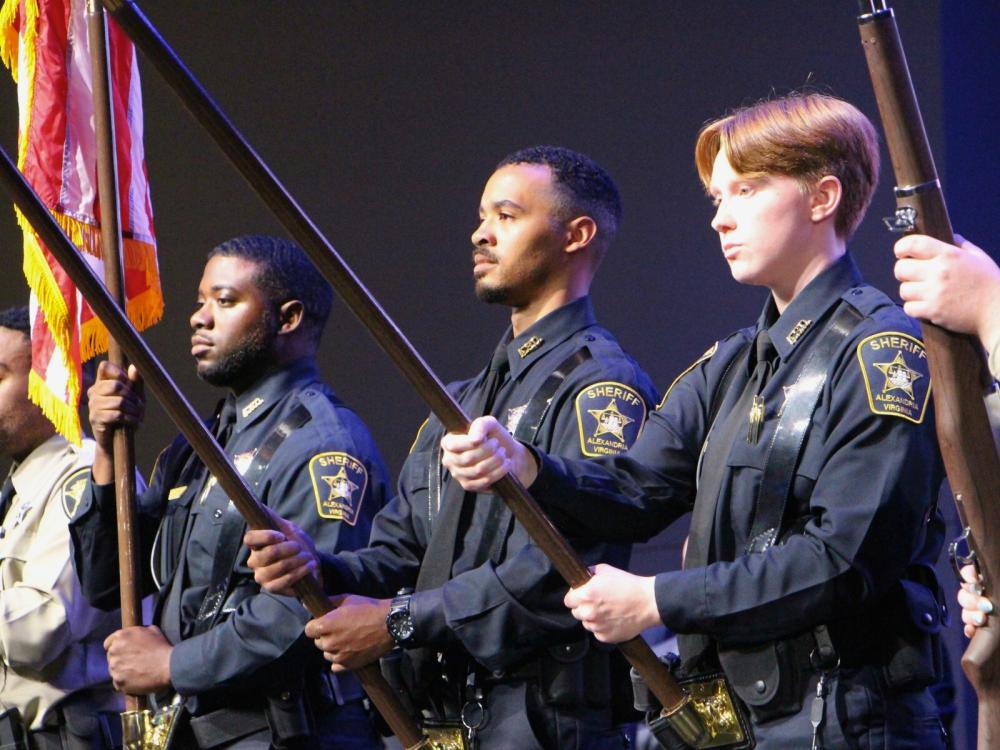 Three deputies in blue uniforms holding flag poles in an honor guard detail