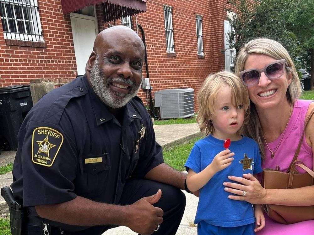 Sheriff's commander in blue uniform with resident and small child at National Night Out, all smiling