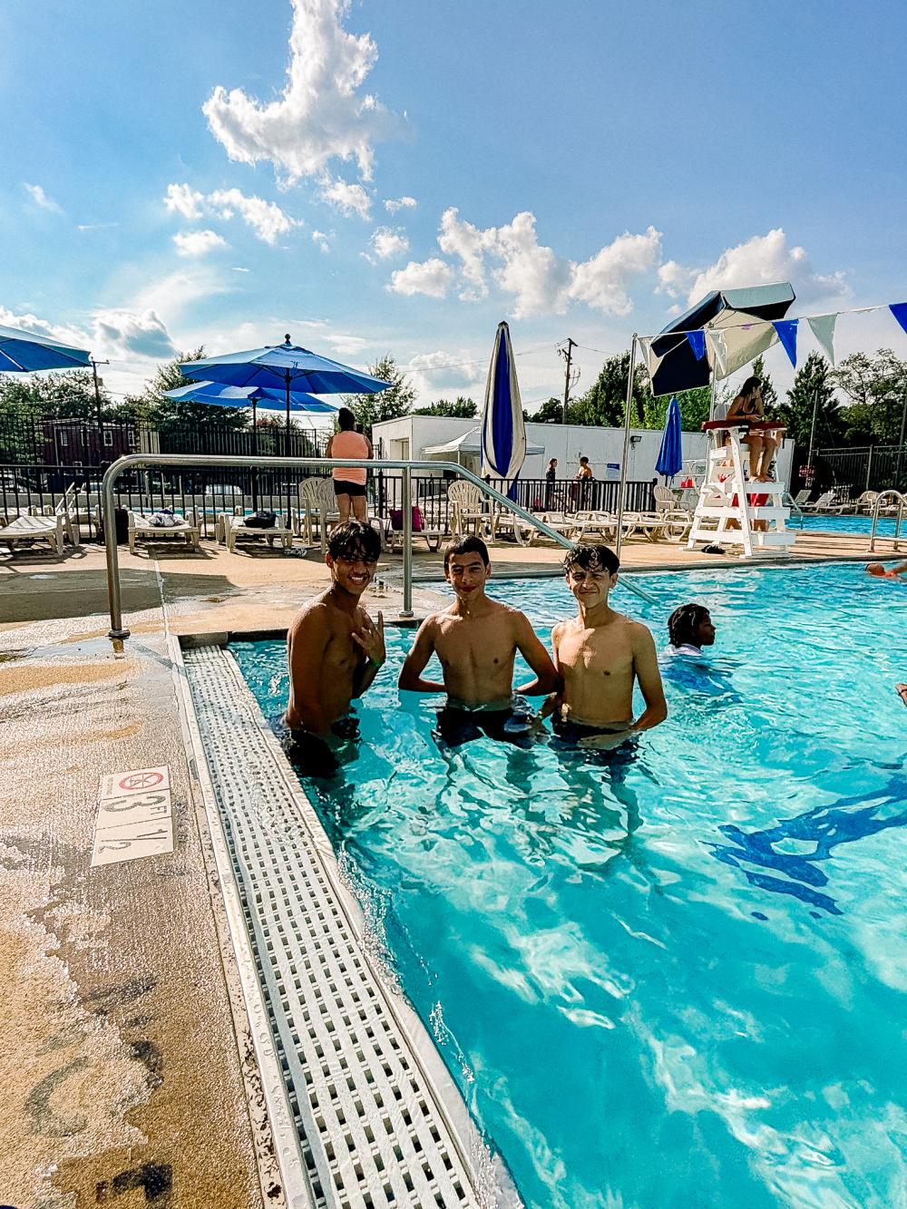 Image of three male teens smiling at the camera while in an outdoor pool