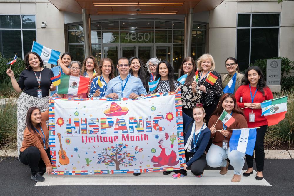 A group of City employees hold a Hispanic Heritage Month banner outside of the Del Pepper Center