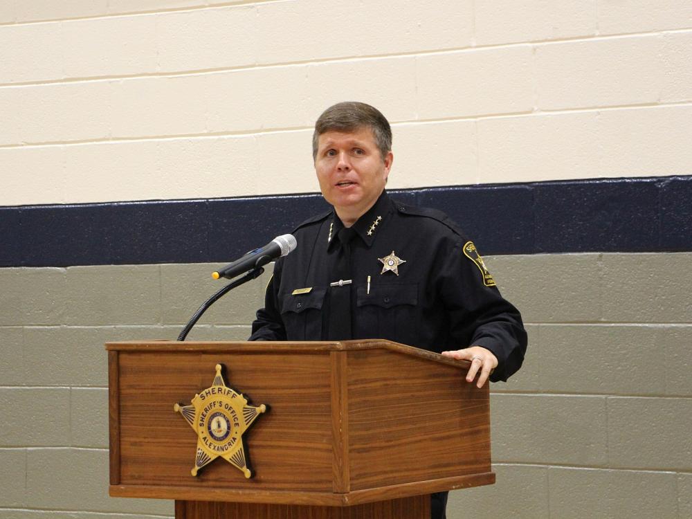 Sheriff in dark blue uniform standing at podium when the Sheriff's Office star on it and speaking into a microphone