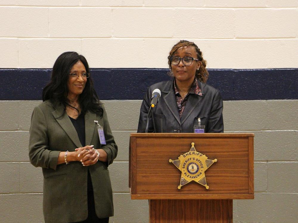 Two judges in business attire standing at podium a the sheriff's office. One is speaking and the other is at her side.