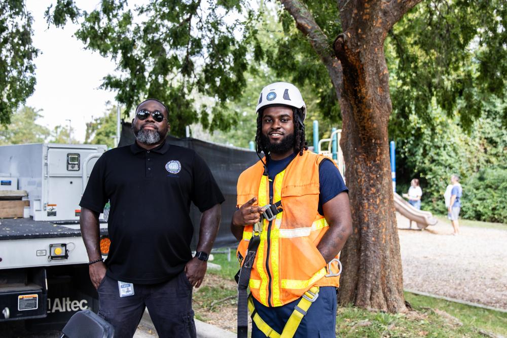 Two city employees smiling in front of trucks