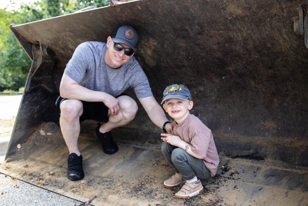 A father and son smiling inside of an excavator bucket