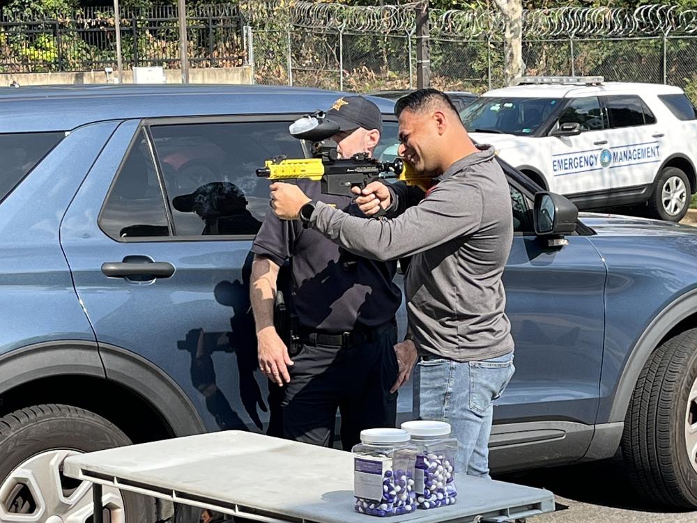 Deputy showing a community member how to deploy a training round in a pepperball launcher