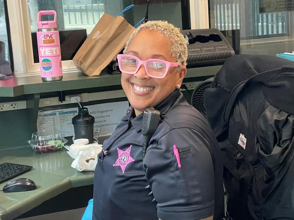 Deputy in a blue uniform with a pink embroidered badge smiling and sitting at her work station