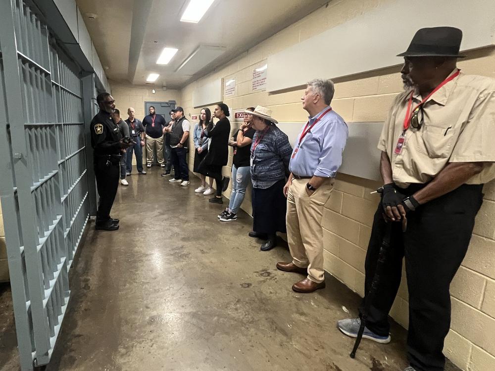 Deputy in blue uniform standing in front of cells speaking with several community members who are opposite the cells