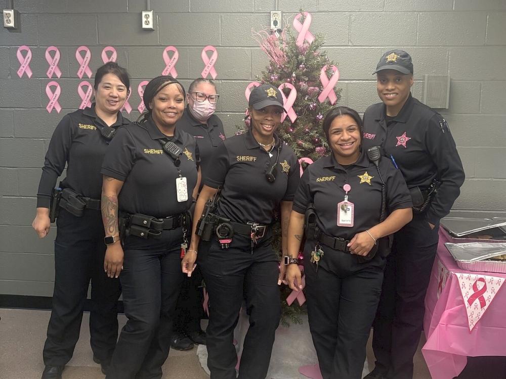 Six deputies, all wearing blue uniforms, with pink ribbons and decorations visible for a brunch for Breast Cancer Awareness Month