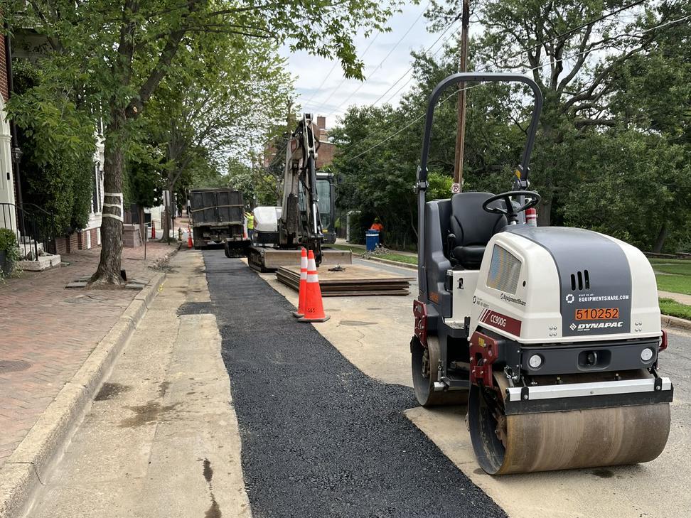 A roller vehicle next to a strip of fresh asphalt on the road.