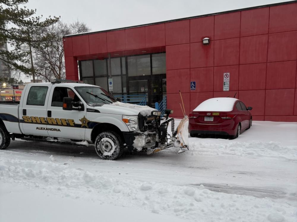 White truck with Sheriff markings and plow blade in snowy parking lot
