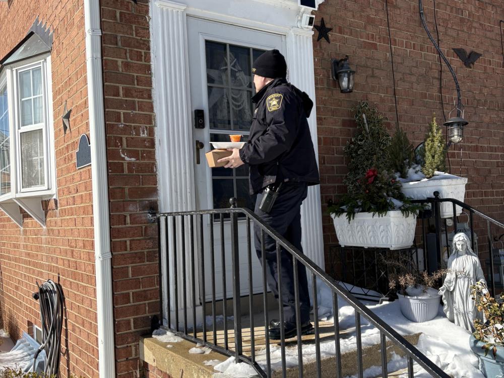 Sheriff in winter uniform delivery meals to a home with snow on the ground