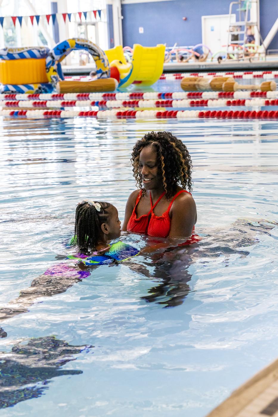 Mother in red swimsuit guiding her daughter in the open swim area of the pool