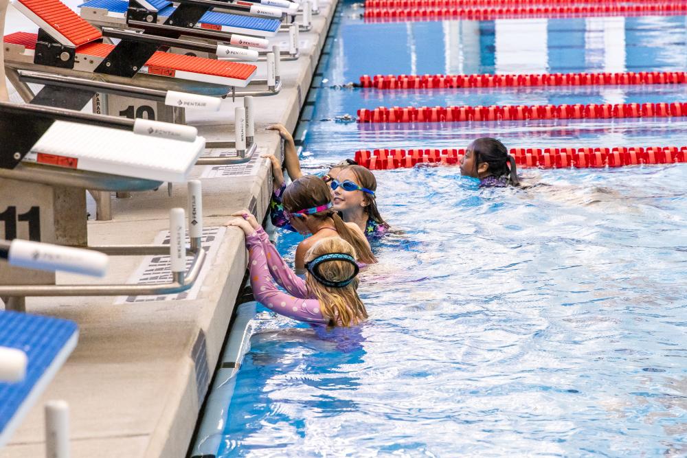 Kids in the deep end of the pool by the diving platforms engaged in a swim class
